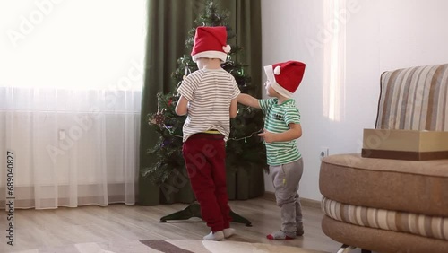 Two little boys, two brothers decorate the Christmas tree at home. Little boys in Christmas caps. A family with children is preparing for the New Year