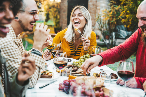 Happy friends having bbq dinner party in garden restaurant - Multiracial young people eating grill meat and drinking red wine in backyard - Food life style concept with guys and girls sitting outdoors photo