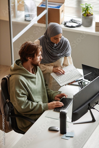 Vertical portrait of IT team of two people reviewing project together in office and using computers photo