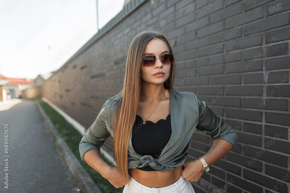 Street beautiful elegant fashion girl with vintage sunglasses in fashionable clothes with a green shirt near a black brick wall. Trendy chic urban woman