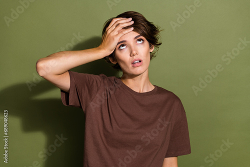 Photo of boring girl with bob hair dressed brown t-shirt hold arm on forehead look up at empty space isolated on khaki color background
