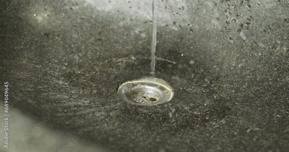 Stream of water flows into drain of sink made of gray stone. Stream of water flows into drain of sink made of gray stone.