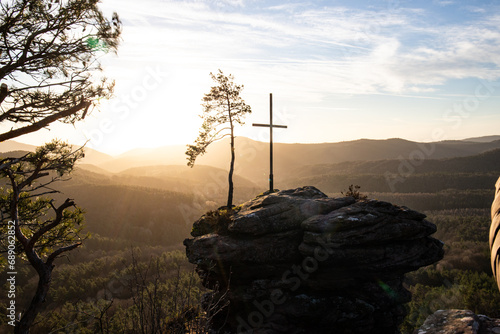 Landscape shot on a sandstone rock in the forest. Morning mood at sunrise at a viewpoint. A small tree and a summit cross stand on the Rötzenfels in the Palatinate Forest, Germany photo