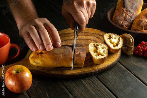 Close-up of a chef hands using a knife to cut a freshly baked apple pie on a kitchen cutting board. The American national dish is served at the holiday table for dinner