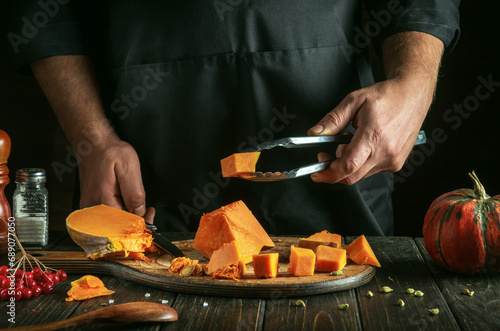 A professional chef prepares diced pumpkin filling for American pumpkin pie. Tool in the hand of a cook with a cube of raw pumpkin. A festive traditional dish popular all over the world