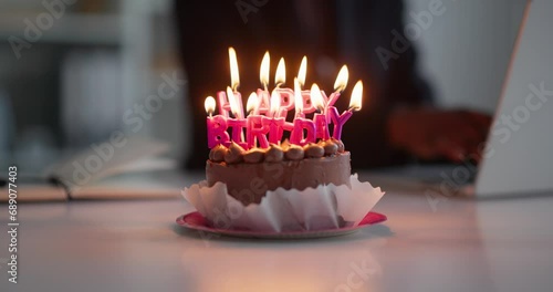 Close up of chocolate birthday cake with burning candles on the desk at office.