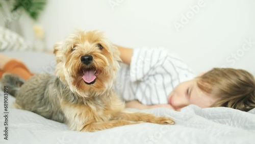 The boy is lying on the bed at home with his dog.