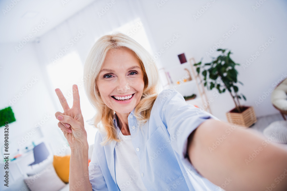Lifestyle blogger selfie photographing mature aged lady makes v sign gesturing peace symbol businesswoman posing indoors living room Lifestyle blogger selfie photographing mature aged lady makes v sign gesturing peace symbol businesswoman posing indoors living room