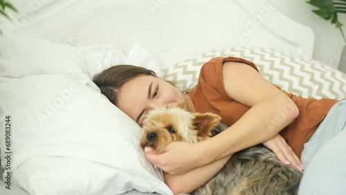 The girl is lying on the bed at home and hugging her Yorkshire Terrier dog.