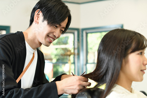 女性客の髪を切るアジア人の男性美容師 © koumaru