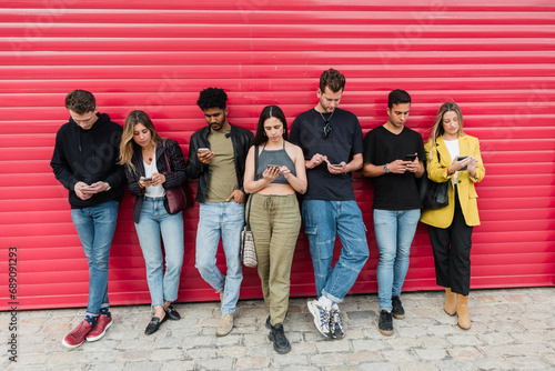 Group of young diverse friends standing near red shutter and browsing smartphone