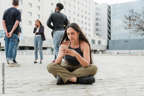 Happy young woman with smartphone sitting with legs crossed on floor near friends