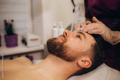 Beautician applying cosmetic mask on man's face in spa salon
