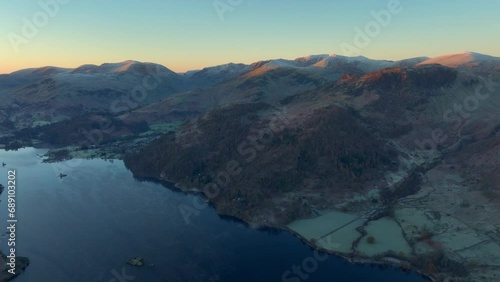 Flying high over dark lake towards sunrise kissed snow dusted mountains in autumn. Ullswater, English Lake District, Cumbria, UK. photo