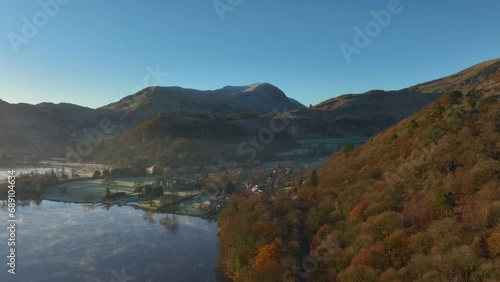 Mist flowing across lake surface towards shore as dawn light shines on autumn wooded hillside. Glenridding, Ullswater, English Lake District, Cumbria, UK. photo