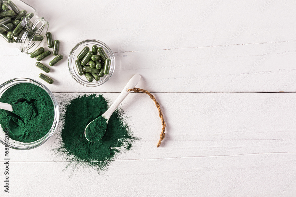 Green spirulina powder, tablets and capsules in various jars on a wooden white table. Top view. A copy space. Biological, natural food additive. Green spirulina powder, tablets and capsules in various jars on a wooden white table. Top view. A copy space. Biological, natural food additive.