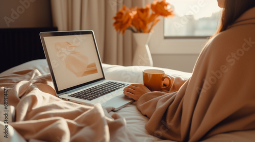 Woman using laptop with coffe mug in bed, work from home 