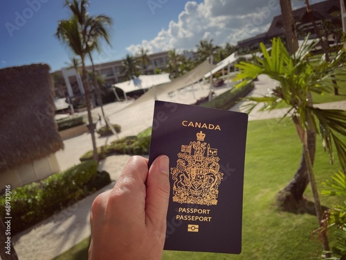main tenant un passeport canadien sur fond de palmiers et de plantes tropicales dans un complexe hôtelier en République dominicaine