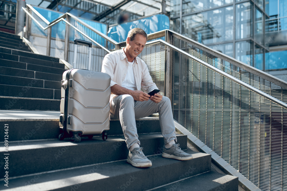 Man with smartphone sitting on stairs with suitcase and using mobile phone after arrival. Man with smartphone sitting on stairs with suitcase and using mobile phone after arrival.