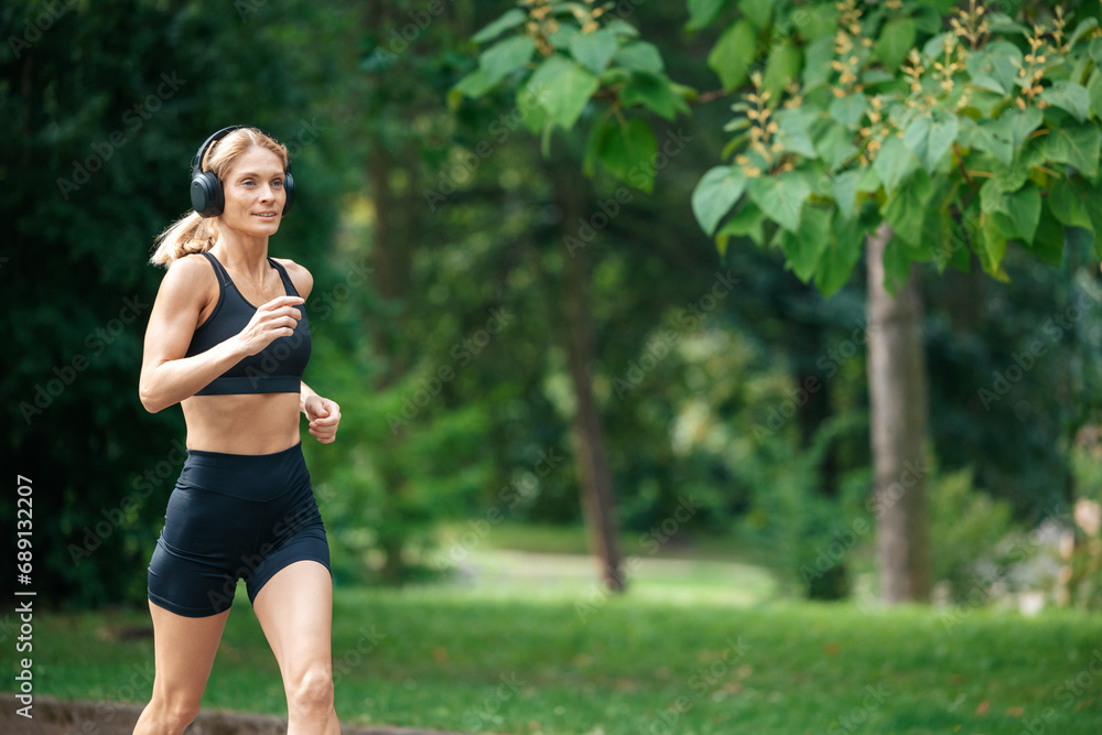 Athletic strong blonde runner woman in headphones jogging in park. Athletic strong blonde runner woman in headphones jogging in park.