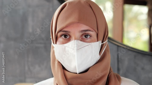 Woman wearing hijab on her head and simple respirator covering mouth and nose. She look straight and steady, confident personnel during pandemic time photo
