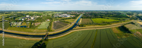 Panorama of solar panels at a sunny day between fields, river and a street.