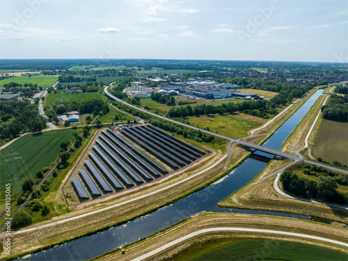 Drone Shot of solar panels at a sunny day between fields  river and a street.