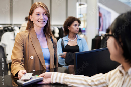 Caucasian girl paying with credit card to cashier at store, another customer standing on background