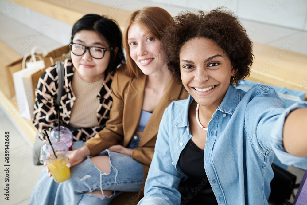 Obraz premium Multiracial group of friends taking selfie together sitting on bench at shopping center