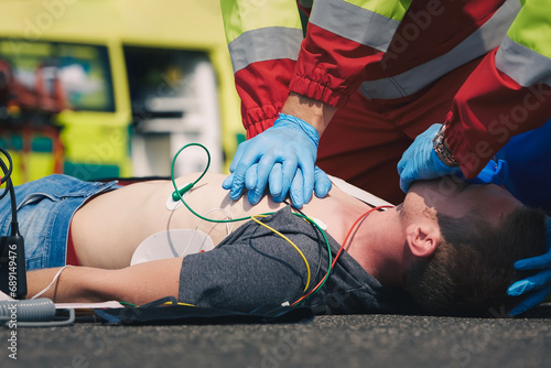 Hands of paramedic and doctor during resuscitation on road against ambulance car. Patient and team of emergency medical service. Themes rescue, urgency and health care..