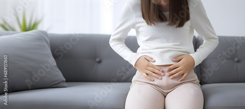 The girl sat on the sofa with her head slumped. His hand clutched his stomach in pain. Abdominal pain with gastritis or menstruation. photo