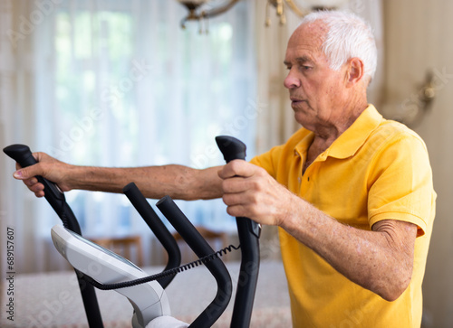 Old man using elliptic trainer at home