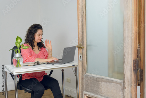 young latin woman with her laptop sitting working on her online business at home.
