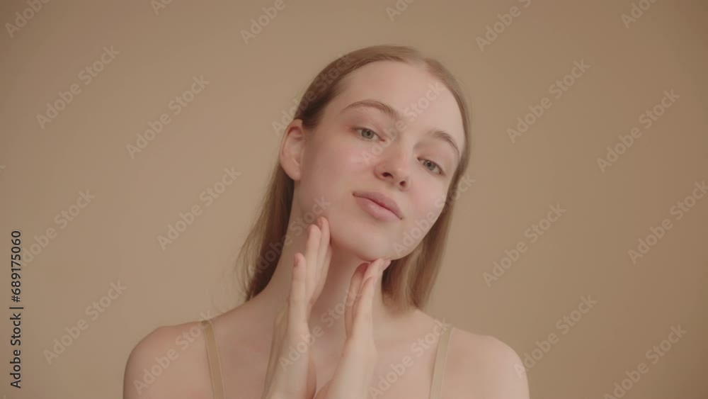 Process of applying a cosmetic product. Young lady looking at camera, enjoying the effect of nourishing face cream application. Portrait of a young Caucasian woman on beige background. Slow motion Process of applying a cosmetic product. Young lady looking at camera, enjoying the effect of nourishing face cream application. Portrait of a young Caucasian woman on beige background. Slow motion