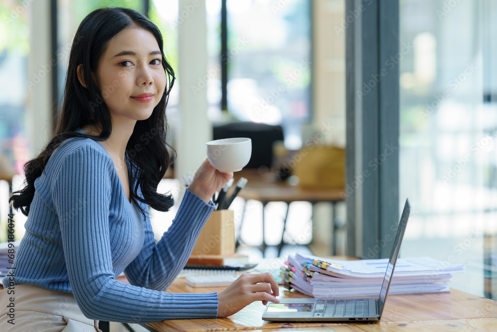 © Songsak C - Beautiful young asian business woman drinking coffee and using laptop computer while working in office. © Songsak C - Beautiful young asian business woman drinking coffee and using laptop computer while working in office.