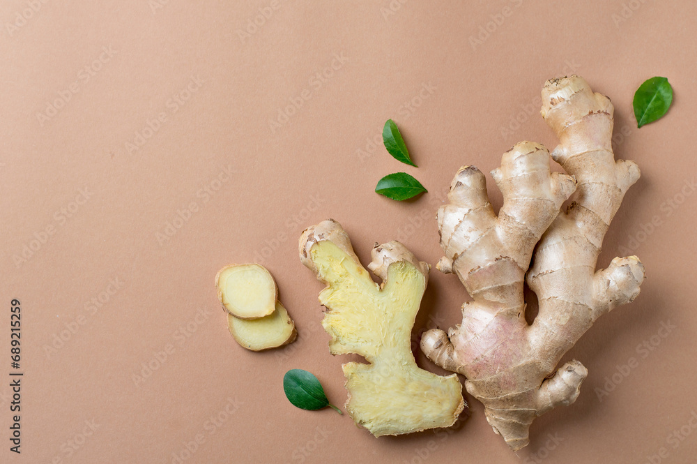 Fototapeta premium Composition of whole and chopped ginger root, green leaves on a light, beige background. Horizontal, free copy space.