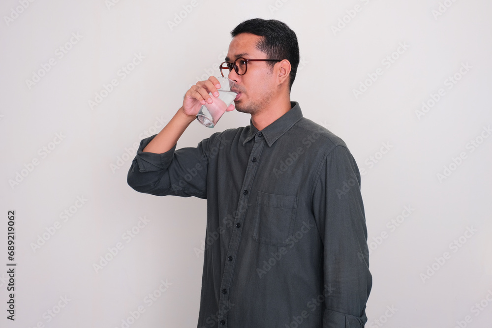Adult Asian man standing while drink a glass of water Adult Asian man standing while drink a glass of water