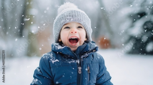Funny excited little boy in blue winter clothes walks during a snowfall. Outdoors winter activities for kids.