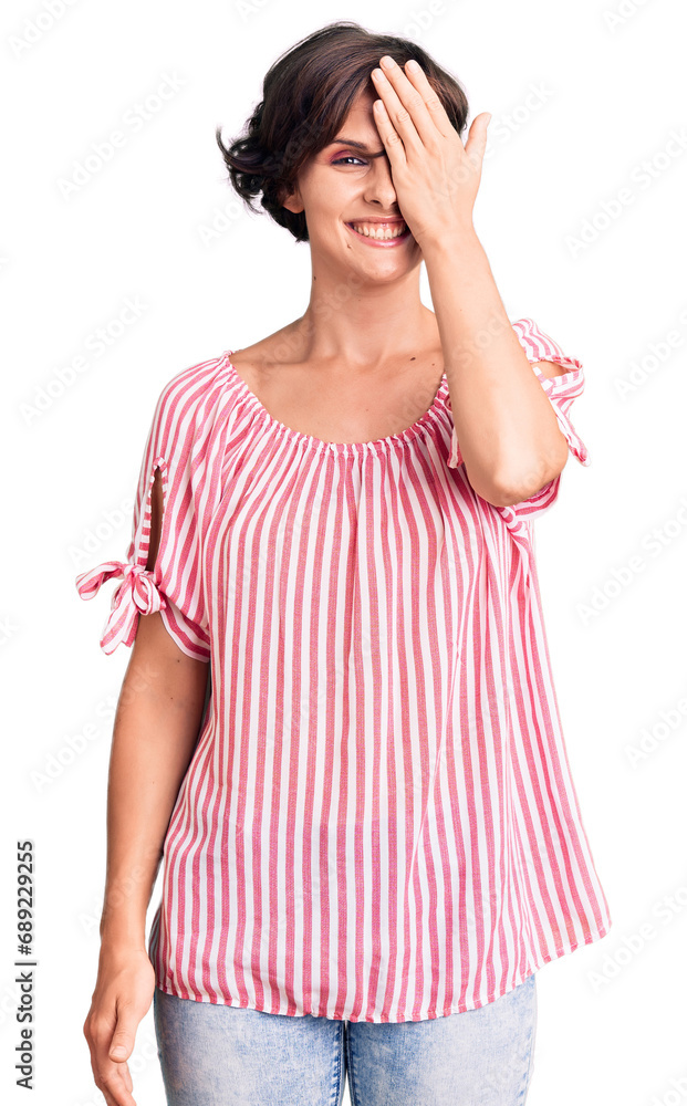 Beautiful young woman with short hair wearing casual summer clothes covering one eye with hand, confident smile on face and surprise emotion. Beautiful young woman with short hair wearing casual summer clothes covering one eye with hand, confident smile on face and surprise emotion.