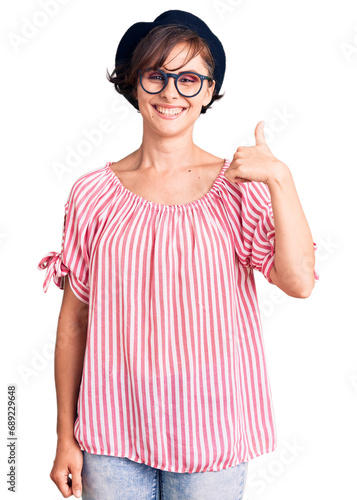 Beautiful young woman with short hair wearing casual clothes and glasses smiling happy and positive, thumb up doing excellent and approval sign