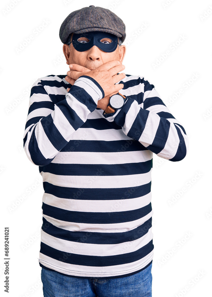 Senior handsome man wearing burglar mask and t-shirt shocked covering mouth with hands for mistake. secret concept. Senior handsome man wearing burglar mask and t-shirt shocked covering mouth with hands for mistake. secret concept.