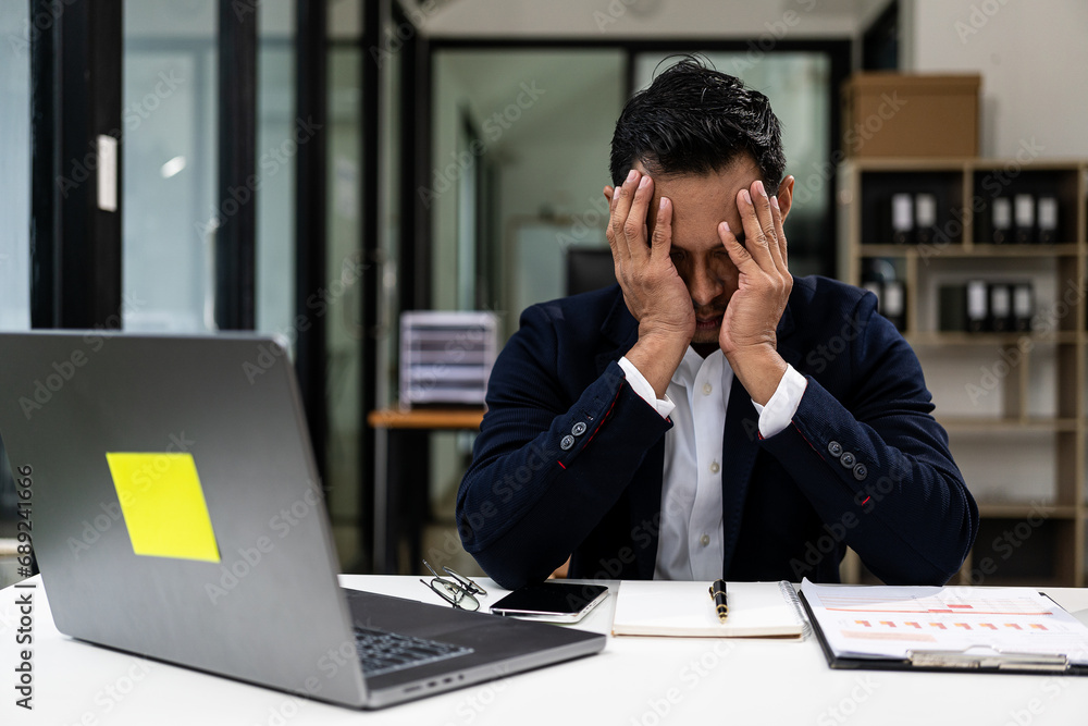 Tired Millennial businessman sitting at laptop touching head feeling tired overworked Suffering from weak eyesight, headache, office syndrome concept. Tired Millennial businessman sitting at laptop touching head feeling tired overworked Suffering from weak eyesight, headache, office syndrome concept.
