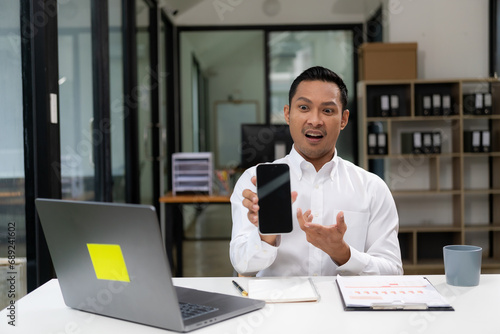 Handsome and happy Asian businessman using his mobile phone at the table Using mobile phone looking at smartphone working in company office with laptop computer technology