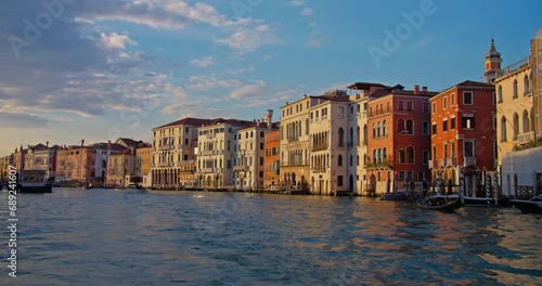 Sunset view of the Grand Canal in Venice, with historical buildings lining the waterway and gondolas docked along the banks. Dusk light casting a warm glow on facades.