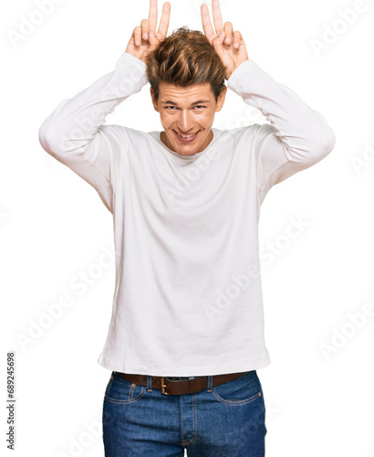 Handsome caucasian man wearing casual white sweater posing funny and crazy with fingers on head as bunny ears, smiling cheerful