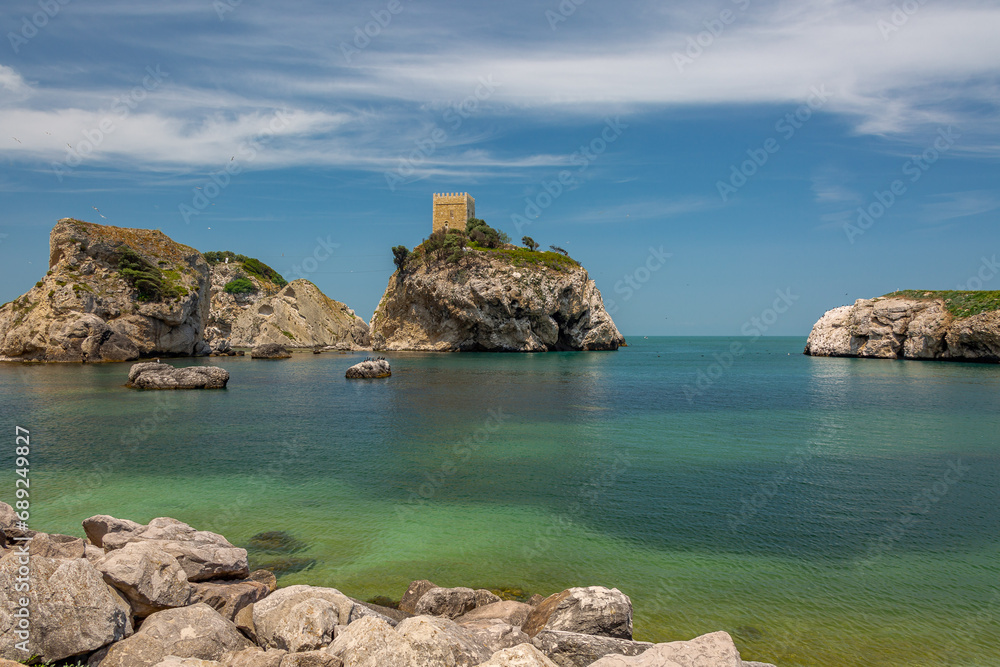 Three small rocky islands against a blue sky. On one of the islands you can see an old stone tower