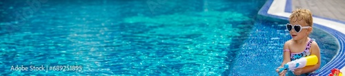 A child plays with a water pistol in the pool. Selective focus.