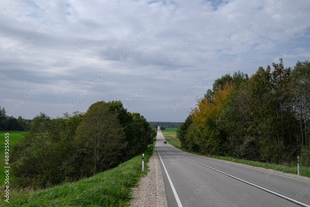straight asphalt road through forest and meadows in Latvia countryside