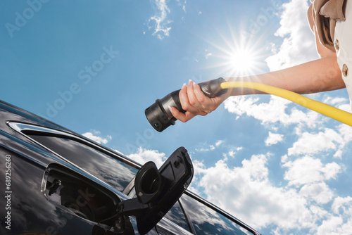 Woman plugging in the charger into electric car at a charging station in the street photo