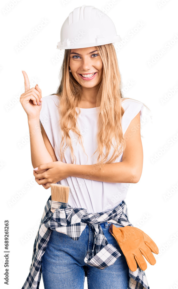 Beautiful caucasian woman with blonde hair wearing hardhat and painter clothes smiling happy pointing with hand and finger to the side Beautiful caucasian woman with blonde hair wearing hardhat and painter clothes smiling happy pointing with hand and finger to the side